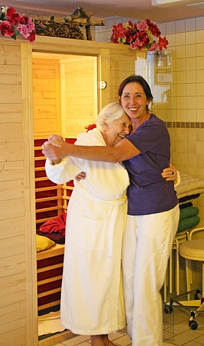 Bewohnerin mit Mitarbeiterin, lachend und Tanzend vor der Sauna