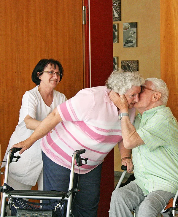 2 Bewohner begrüßen sich herzlich, im Hintergrund eine Mitarbeiterin