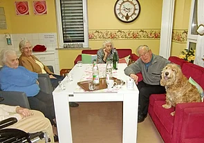 Bewohnerin in einem Gemeinschaftsraum am Tisch, mit dabei ist ein Hund